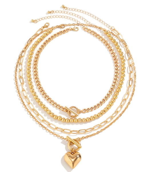 Collier multicouches doré avec cœur  4 chaînes dorées superposées de styles différents (maille gourmette, perles, maillons) avec un pendentif cœur. Look moderne empilé.